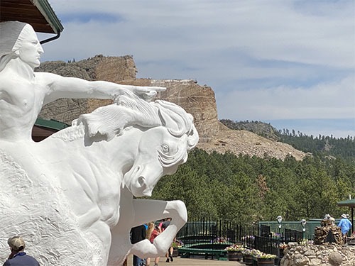 Completed scale model of Chief Crazy Horse on his horse in front of the partially completed sculpture on the mountain