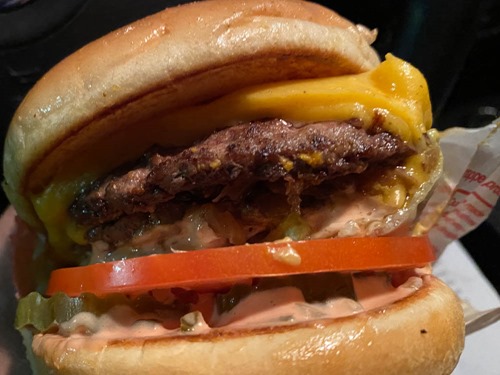 Closeup of a double cheeseburger with a slide of tomato, pickle chip, and Thousand Island dressing visible.