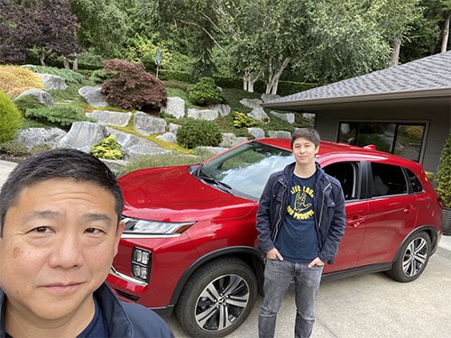 Selfie of Tony and Andrew in front of a bright red Mitsubshi Outlander SUV