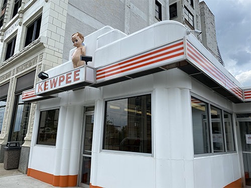 A small white square art deco building with a Kewpee sign and a Kewpee doll over the sign.