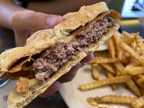 Image of the burger sliced in half. The meat is medium rare, the bun is prett flattened. There is cheese above and below the patty.