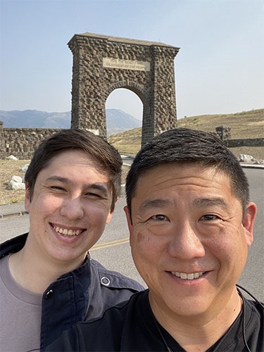 Andrew and Tony in a selfie in front of a rough brown stone arch