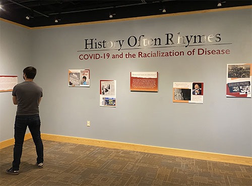 Andrew reading a museum exhibit wall with the title 'History Often Rhymes" and the subtitle "COVID-19 and the Racialization of Disease"