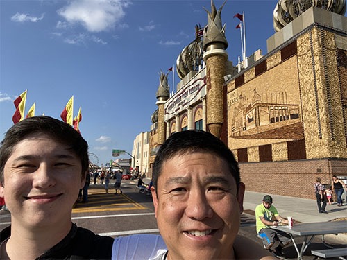 Selfie of Andrew and Tony in front of a palace-like building covered in murals made from corn.