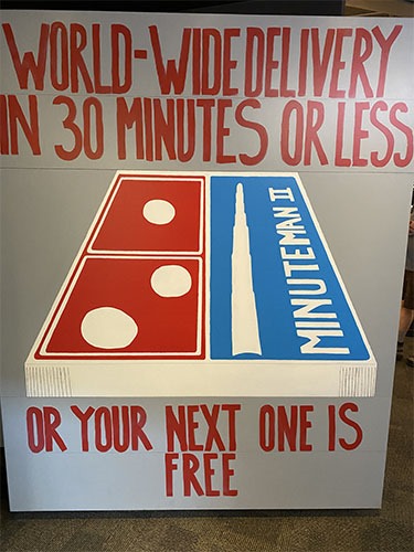 Mural saying "World-wide delivery in 30 minutes or less or your next one is free" and a Domino's pizza box with a Minuteman II label and image on it.
