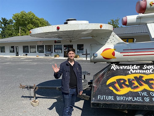 Andrew standing next to a parade float of a starship in front of a small stripmall museum. He is giving the Vulcan "live long an prosper" salute.
