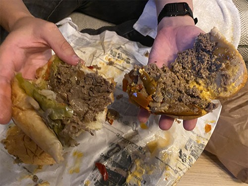 Two cheesesteak sandwich halves, open. The one of the left has slices of beef. The one on the right has almost chopped beef.