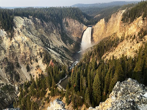 A tall waterfall spilling into a valley with bare rock and tall trees
