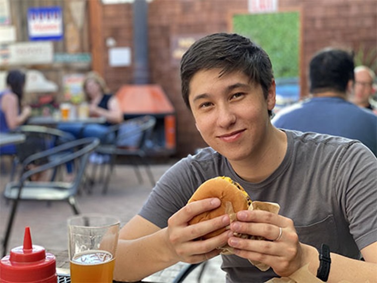 Andrew holding his burger, sitting on an outdoor patio, beer and ketchup in front of him