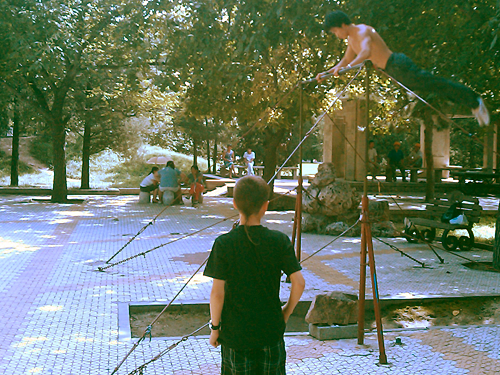 Ripped dude doing a big swing on a high bar as Andrew looks on.