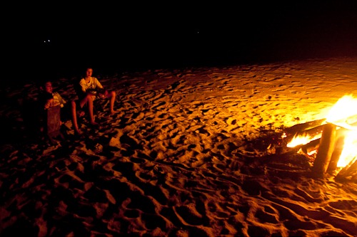 Kids sitting near the huge fire on the beach.