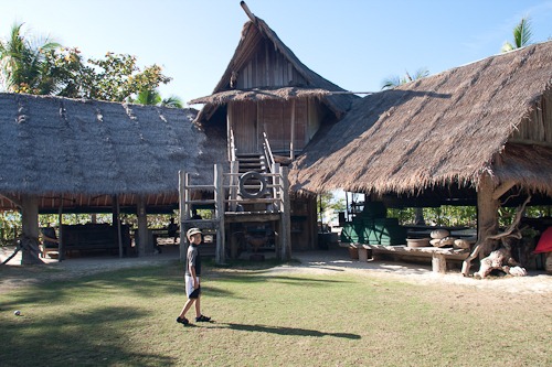 Michael standing in front of a two story thatched roof building with open sides.